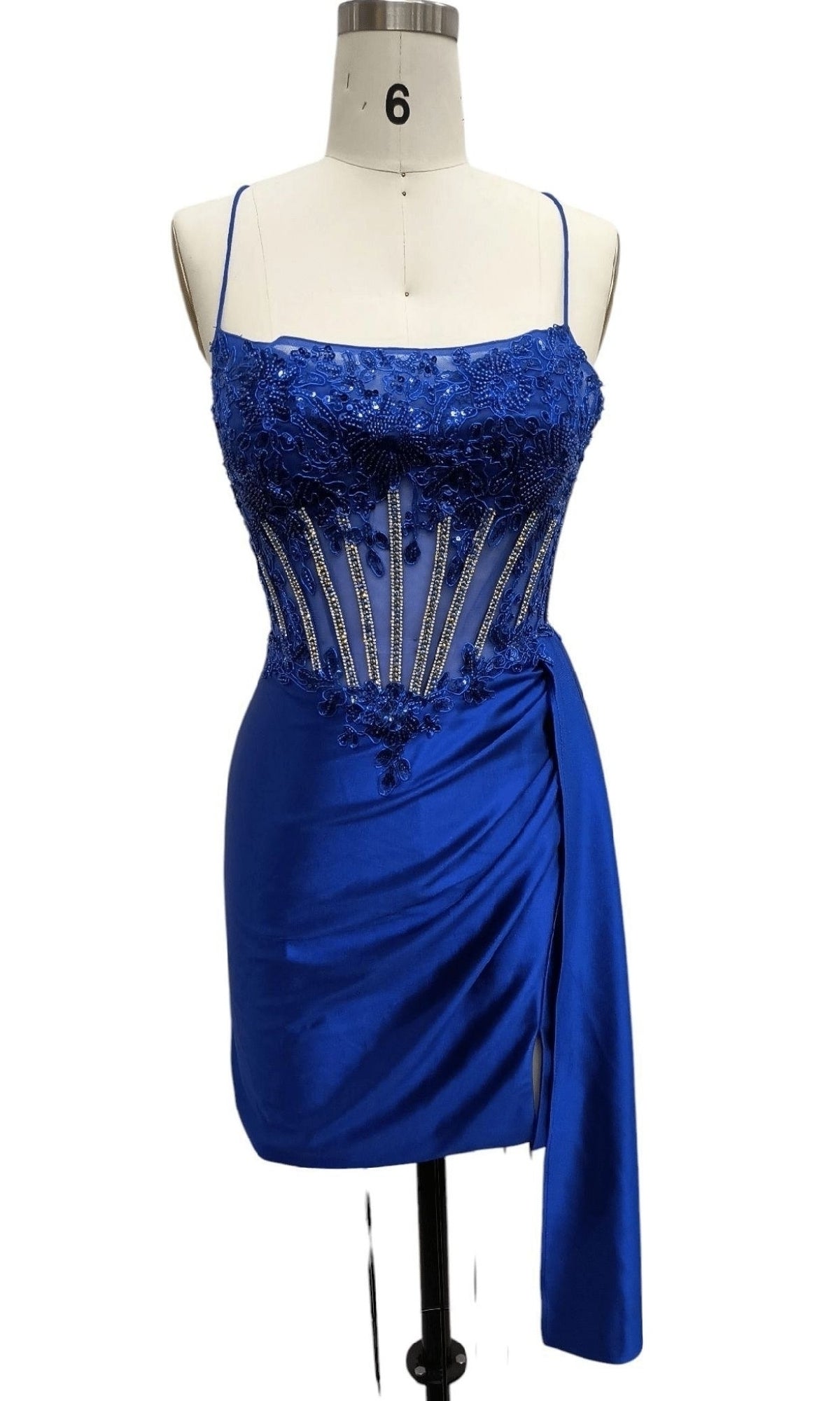 A mannequin showcases the Lace-Up Short Hoco Dress 12659, a royal blue party dress with a beaded sheer corset bodice, spaghetti straps, and an asymmetrical draped skirt—perfect for homecoming.